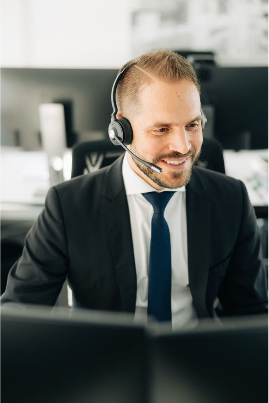 An agent in a headset at his desk, smiling at his screen.