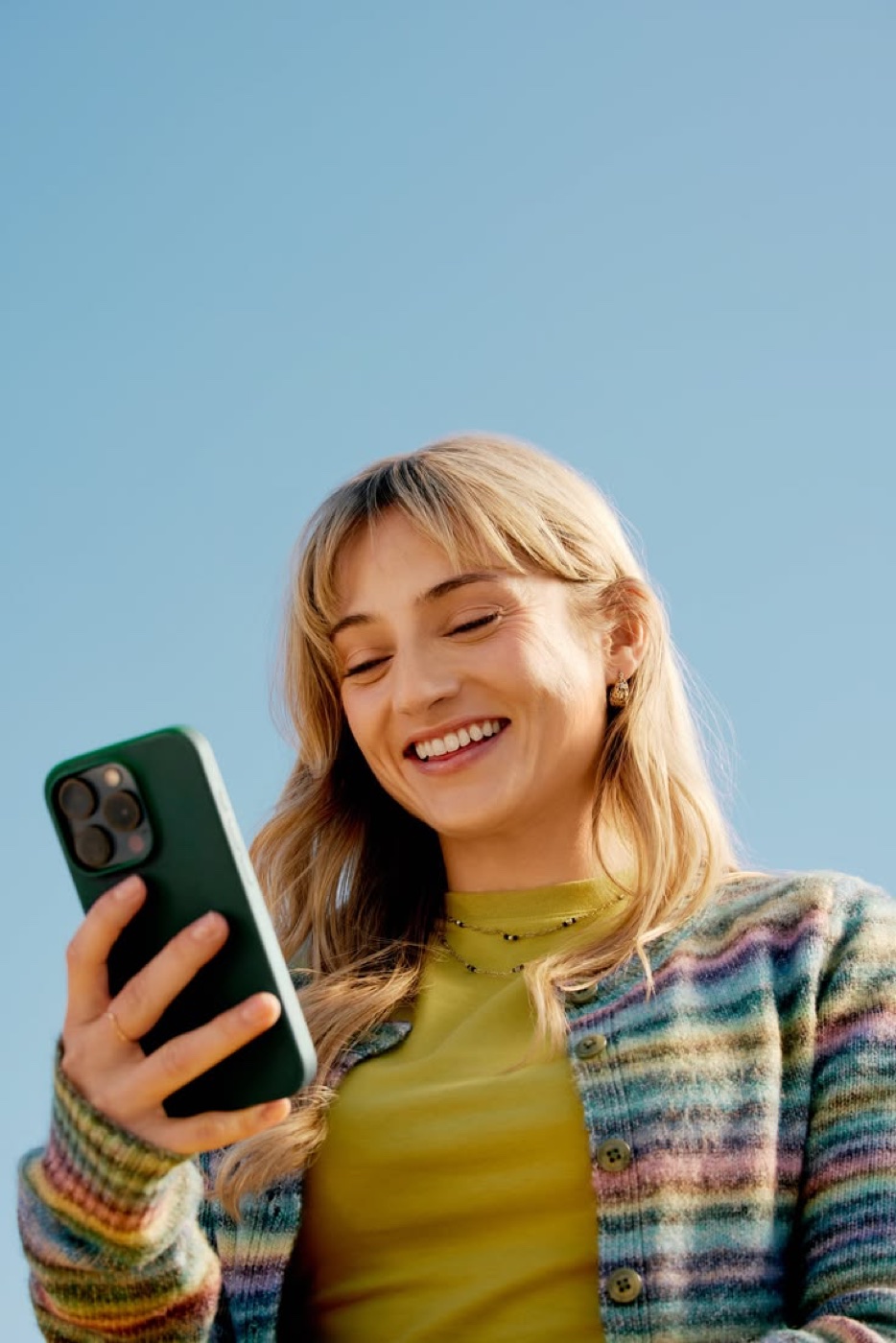 A customer outdoors, smiling at her phone.